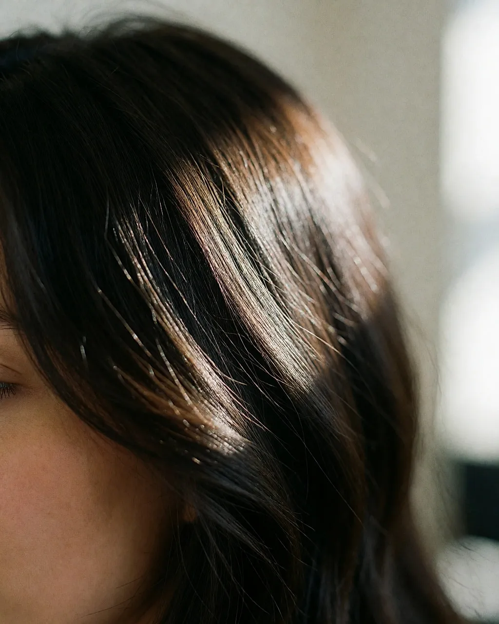 Détail de cheveux bruns brillants traversés par la lumière d'une fenêtre