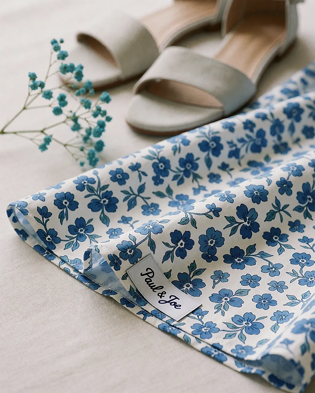 Weißer Baumwollstoff mit kleinen blauen Blumen, Saum und Etikett sichtbar