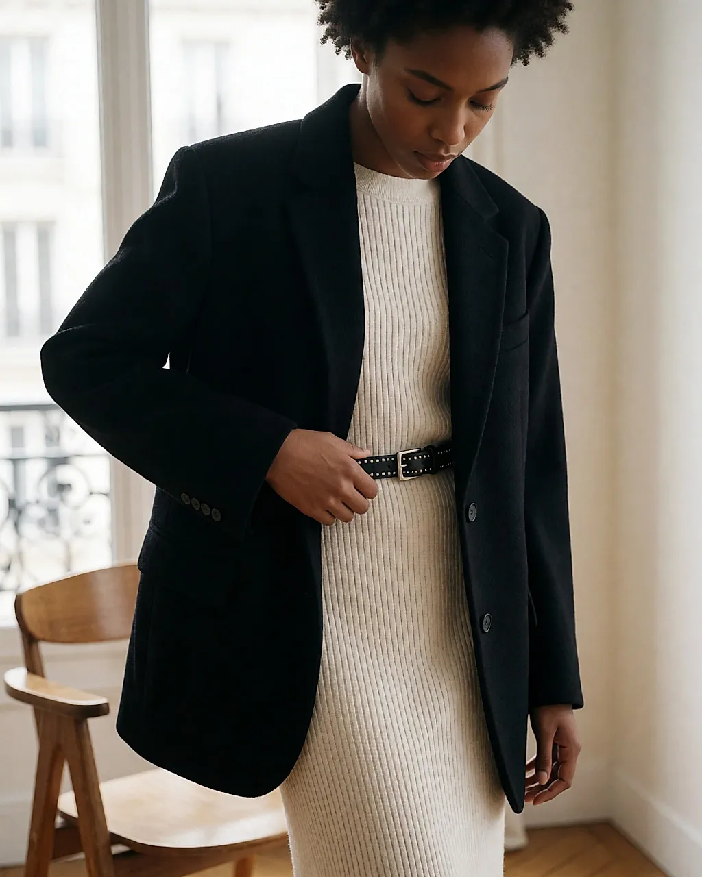 A woman adjusting a fine studded belt over a knitted midi dress and an oversized blazer