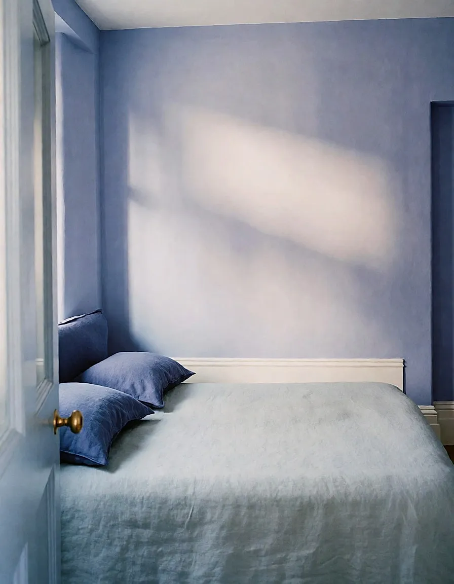 Schlafzimmerecke in Lavendelblau mit Leinenbett und indigofarbenen Kissen