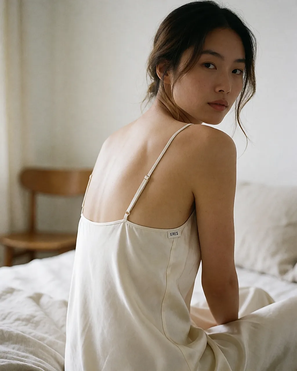A woman wears a silk-satin Eres nightdress by a bedroom window