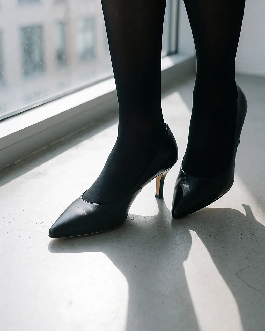 Detalle de dos pies con zapatos de salón negros de tacón fino sobre un suelo de hormigón claro
