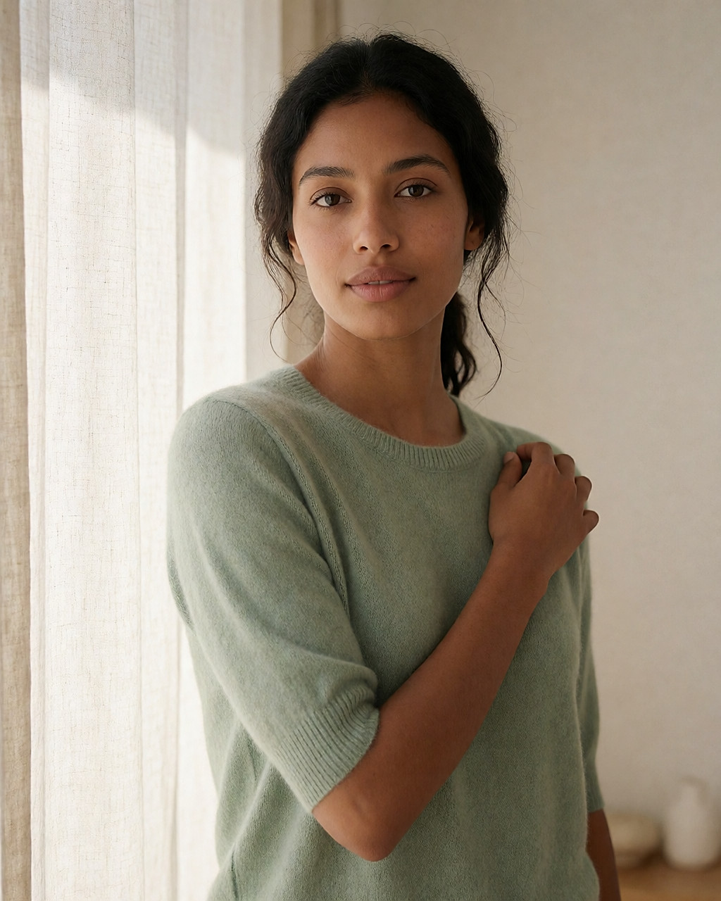 Young woman in a sage knit top adjusting her top in a bright fitting room