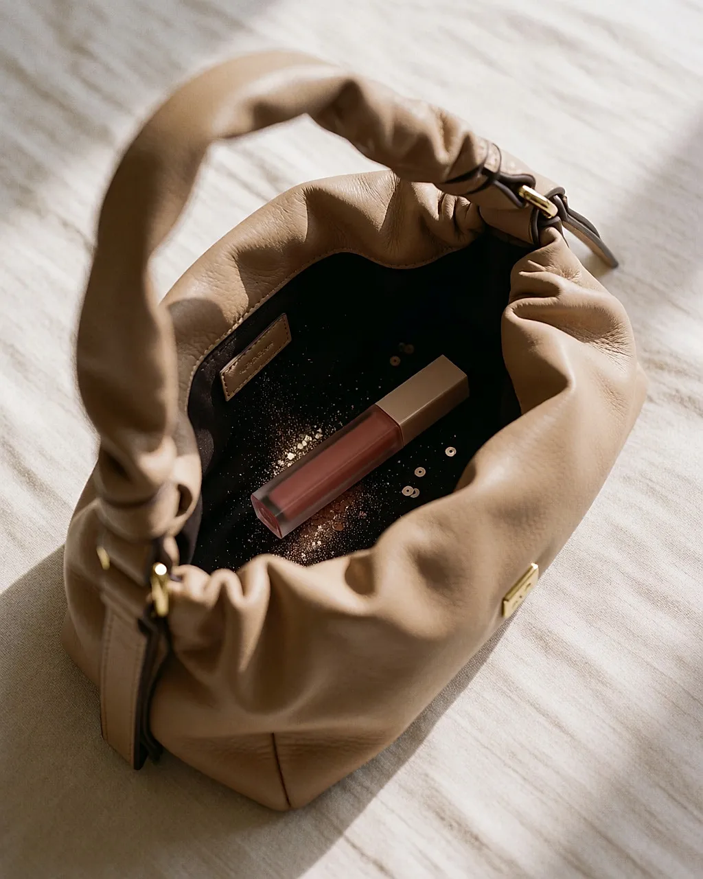 Open bag on a bed, a lip gloss tube and fine glitter on the lining