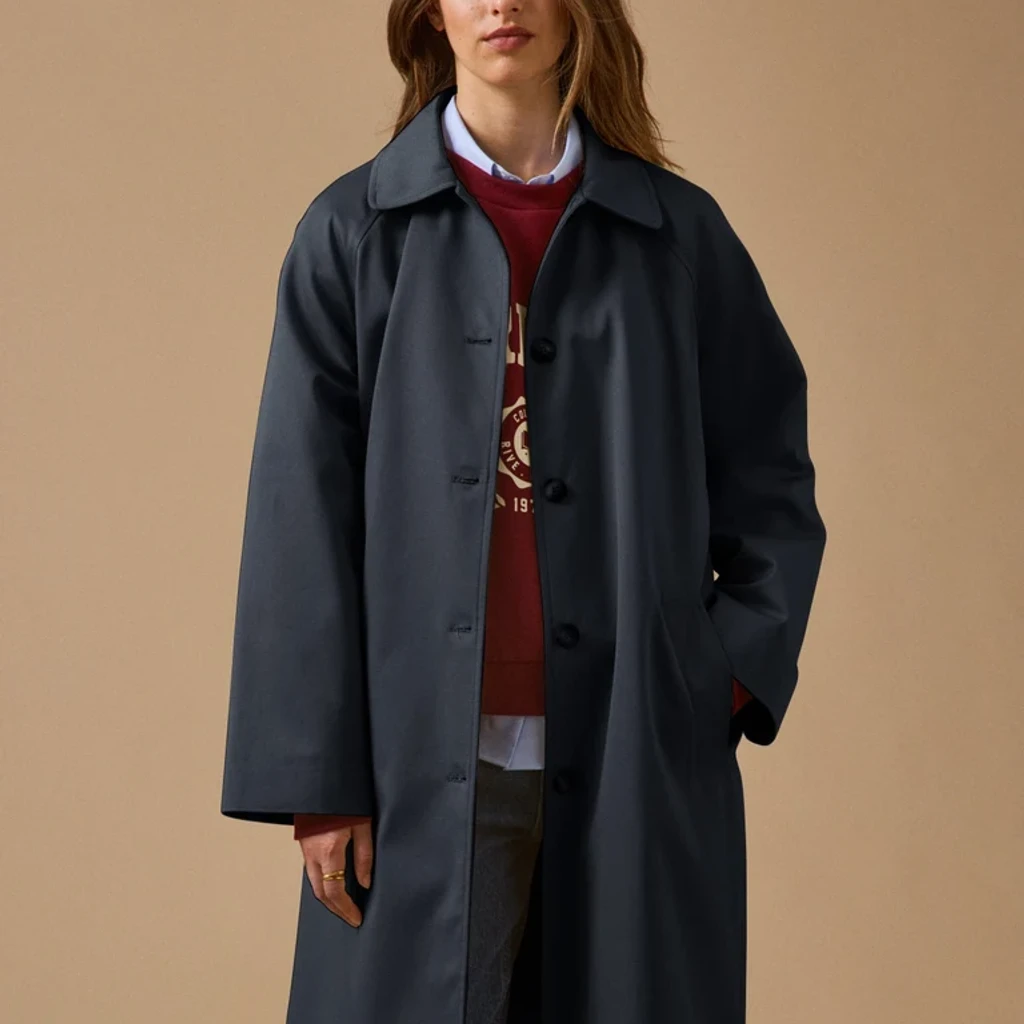 Ein gerade geschnittener Trenchcoat aus Bio-Baumwolle, gegürtet getragen, in einer baumgesäumten Allee
