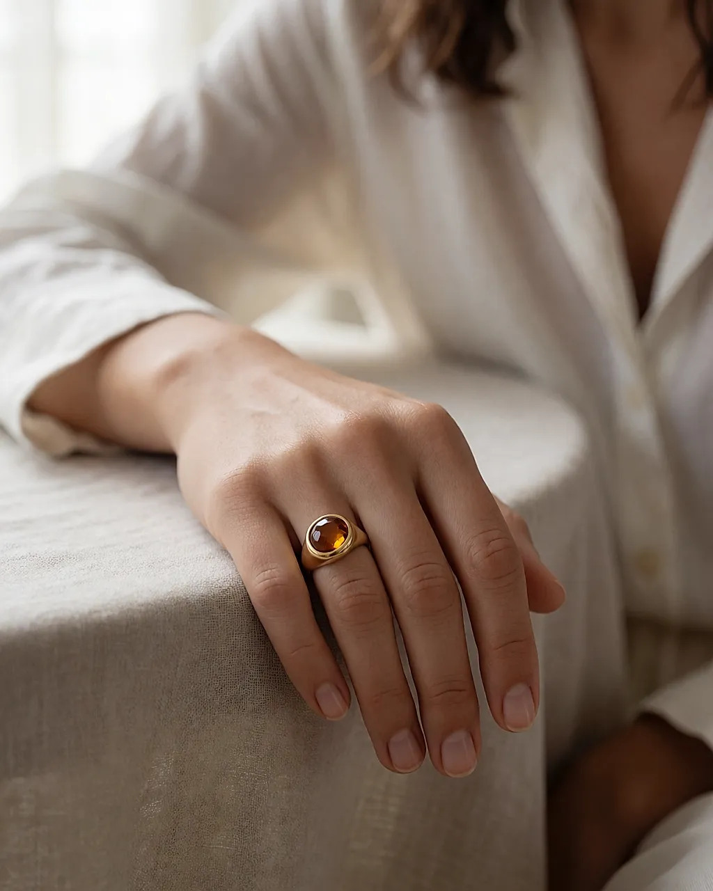 Goldener Ring mit Cabochon aus bernsteinfarbenem Glas an einer Hand auf Leinen