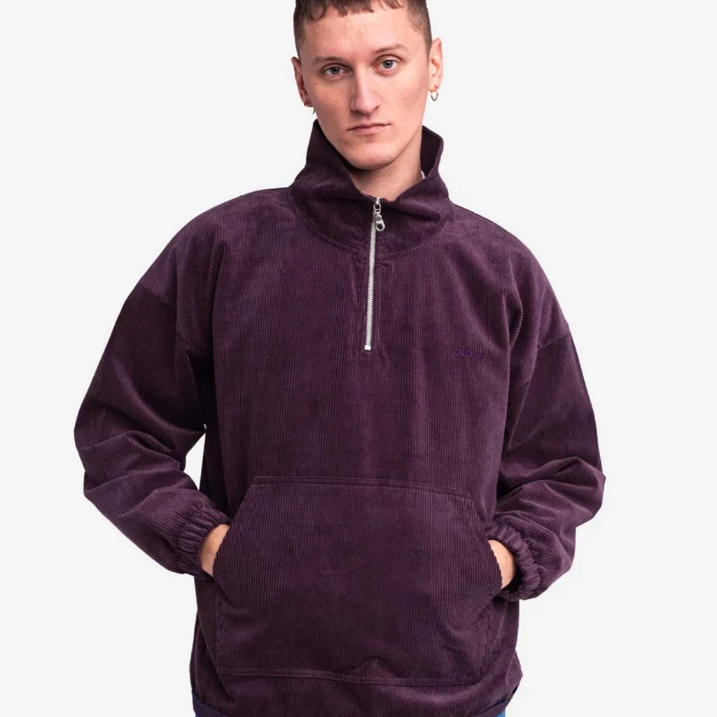 Costas de uma jovem com sweatshirt de veludo ameixa e calças de cintura baixa num quarto claro