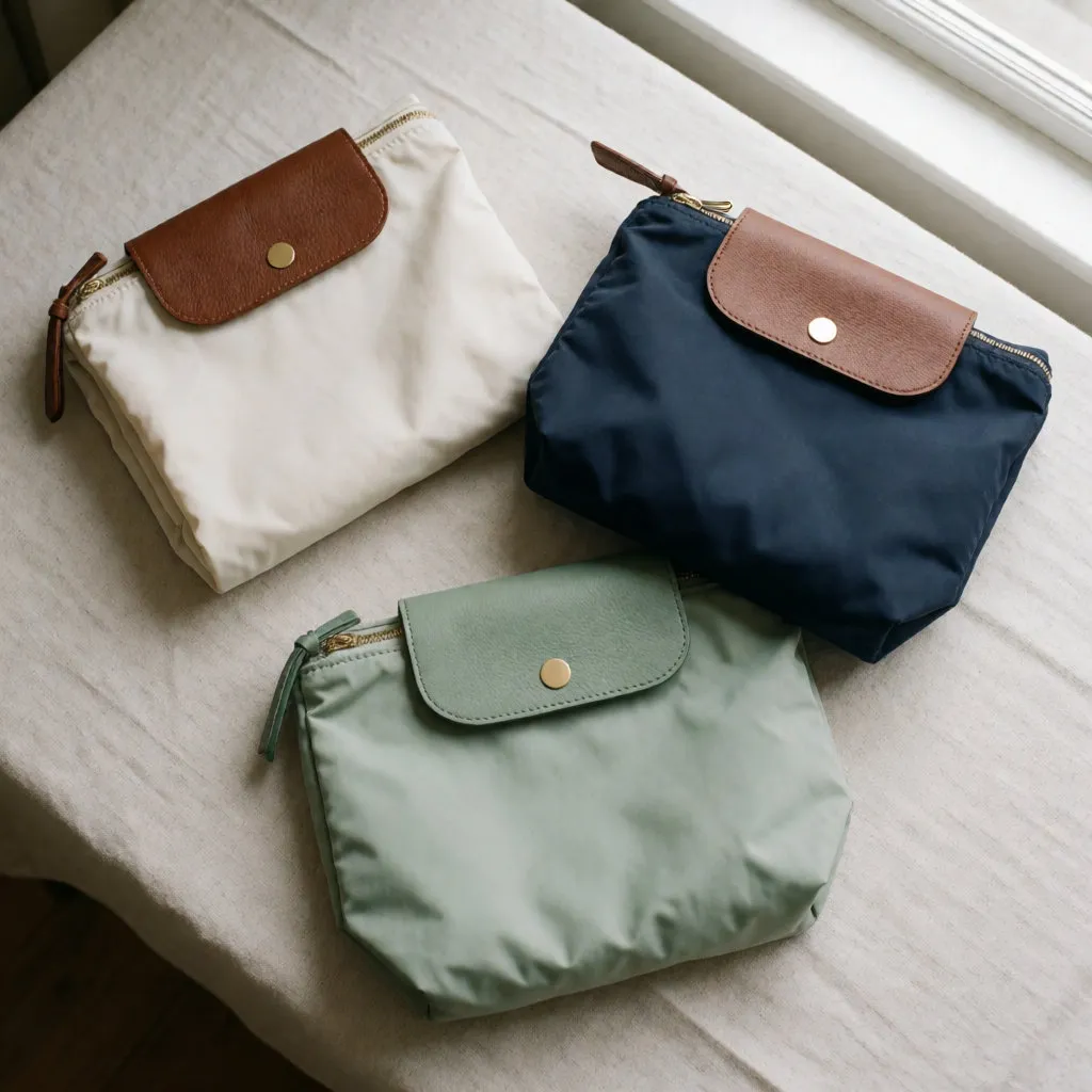 Tres bolsos plegables de nailon con solapas de cuero, alineados en plano sobre una tela de lino clara