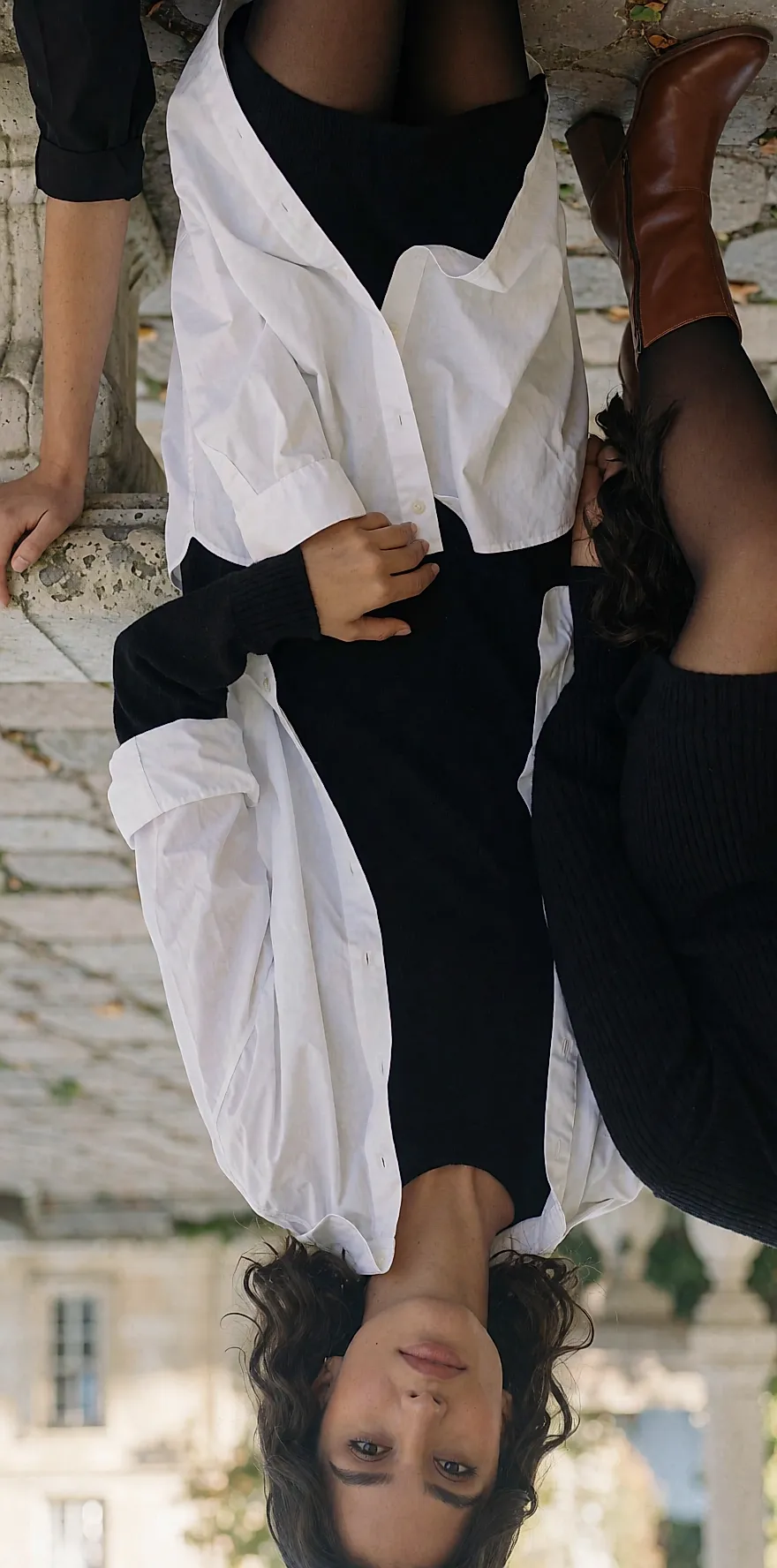 Oversize white shirt left open over a black knit dress, worn in a courtyard