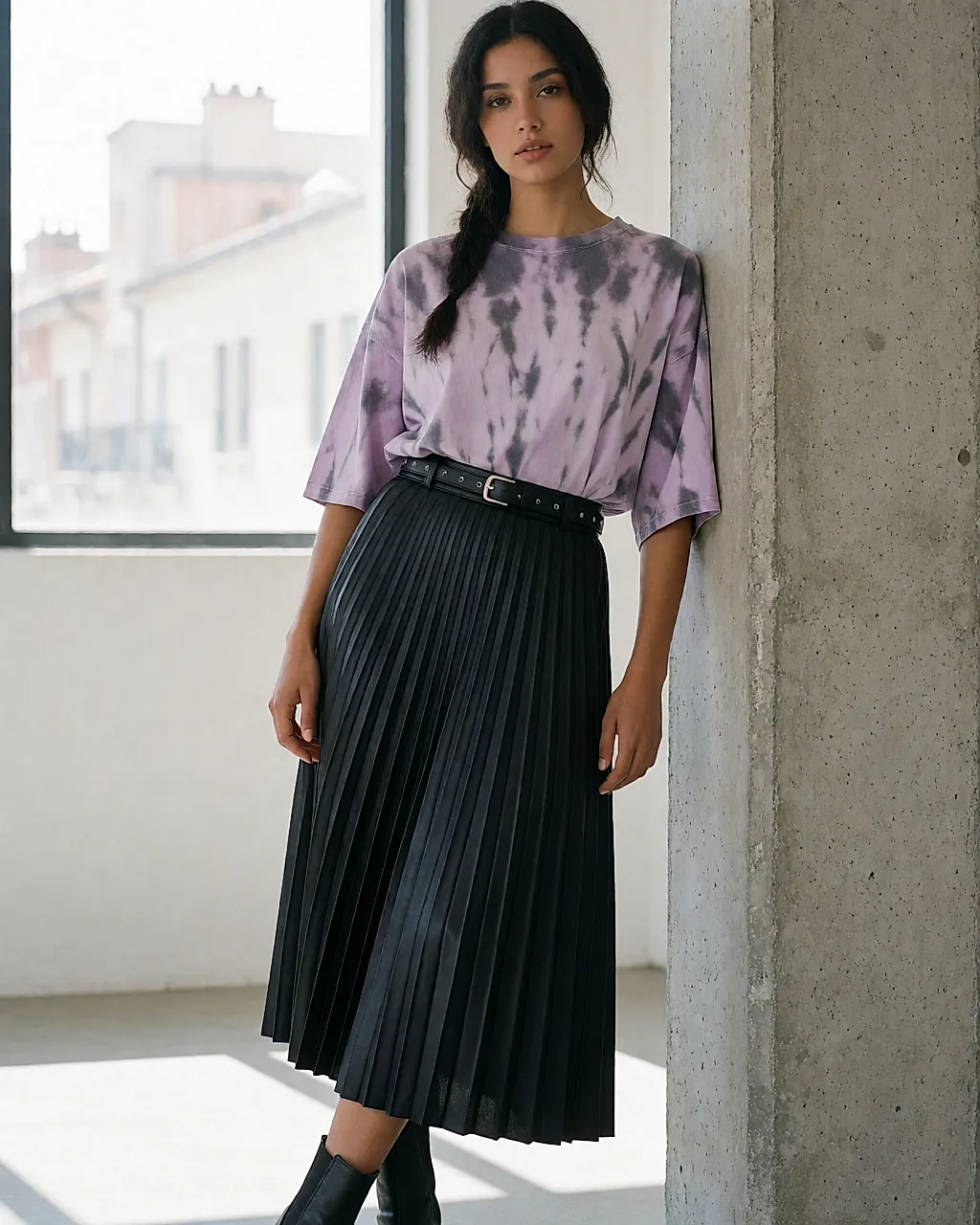 Junge Frau in plissiertem Midirock aus Kunstleder und gegürtetem Tie-Dye-Shirt