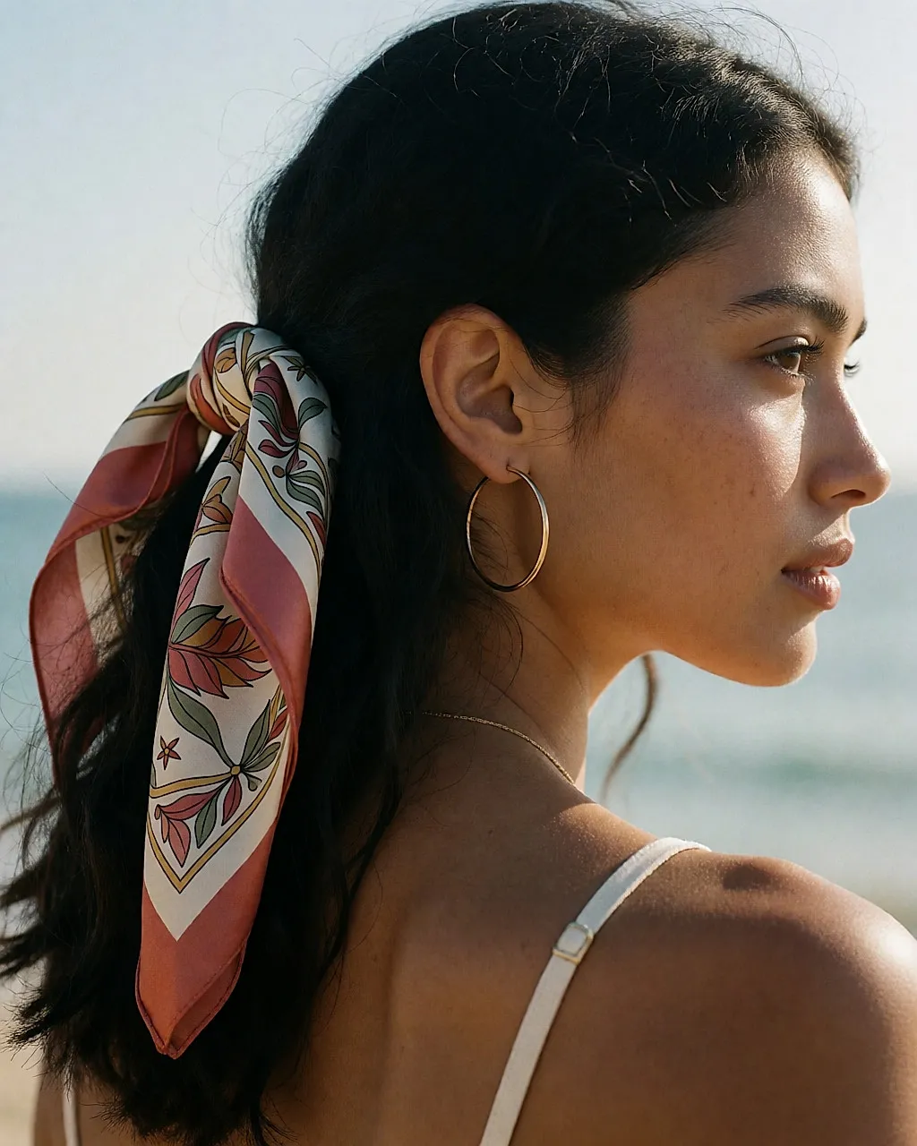 Foulard en soie noué dans les cheveux et créoles dorées, vue de trois-quarts arrière
