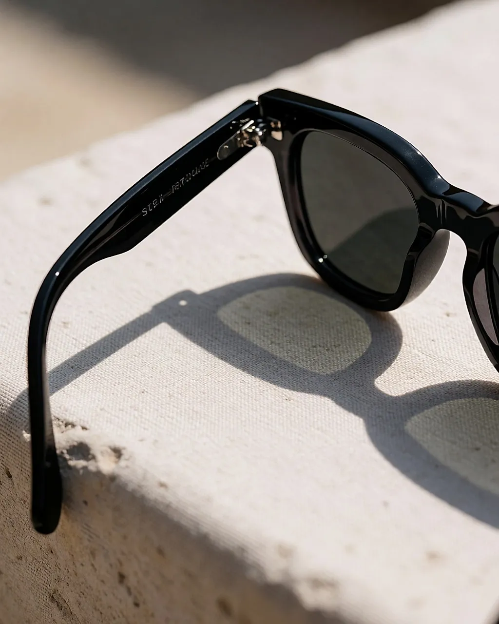 Nahaufnahme von Gestell und Scharnier einer Sonnenbrille auf hellem Leinen