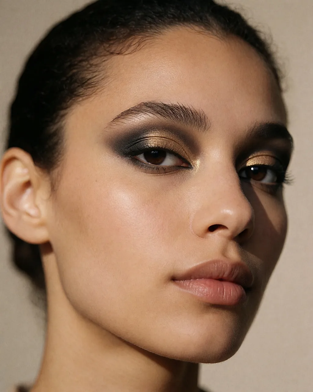 Finger, der einen goldenen Lidschatten in die Mitte des Lids tupft, über einem nach außen verblendeten schwarzen Smokey-Look