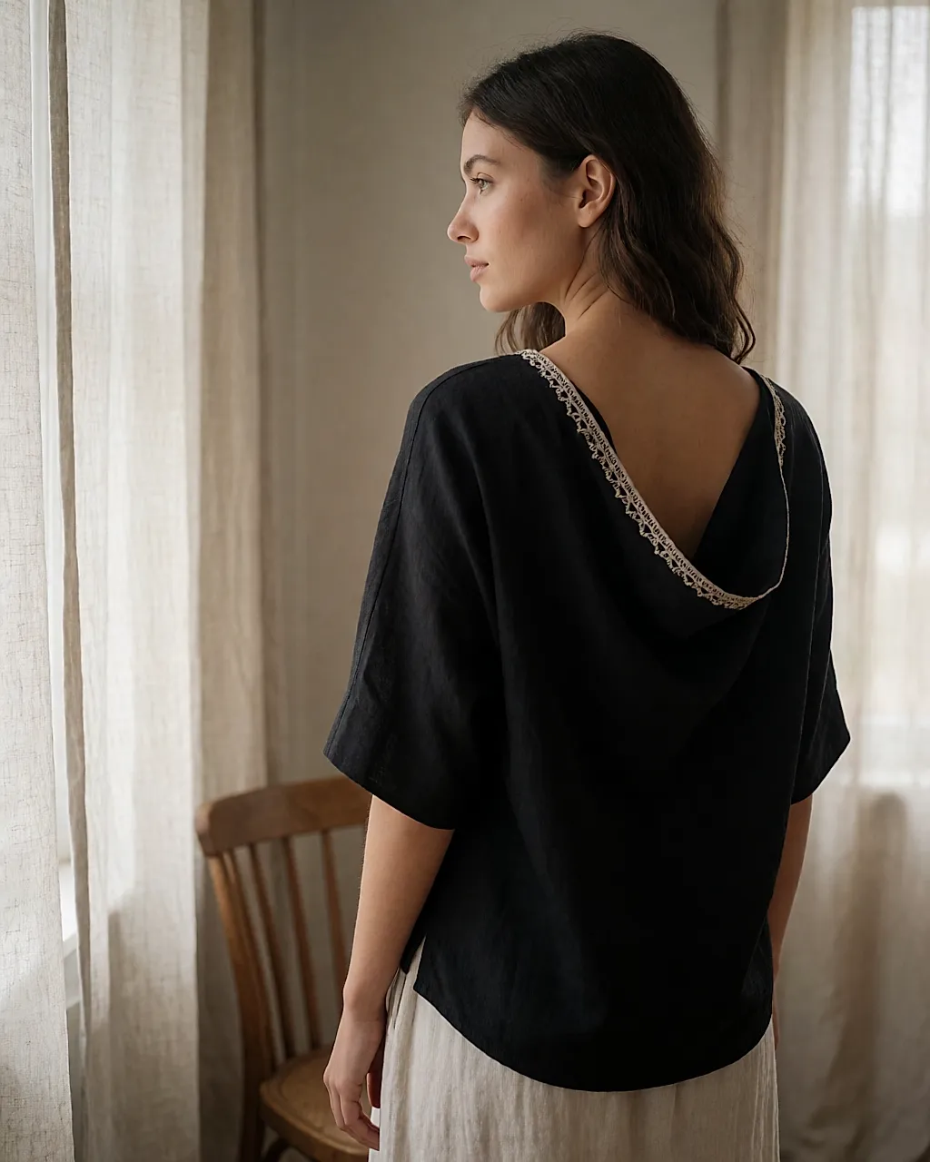 Back view of a draped black top with embroidered trim worn by a young woman