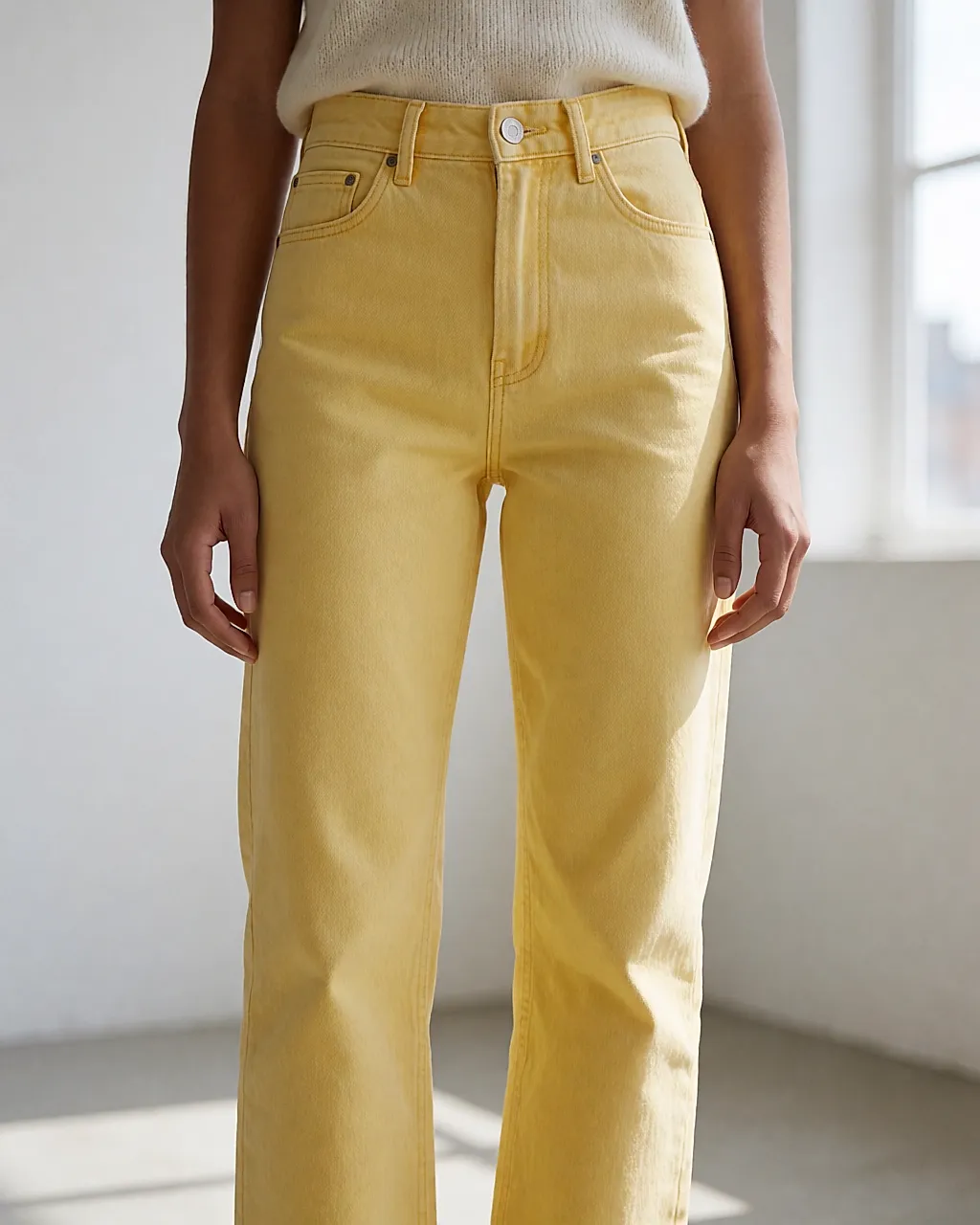 Yellow jeans worn with a tucked-in cream jumper, framed on the legs