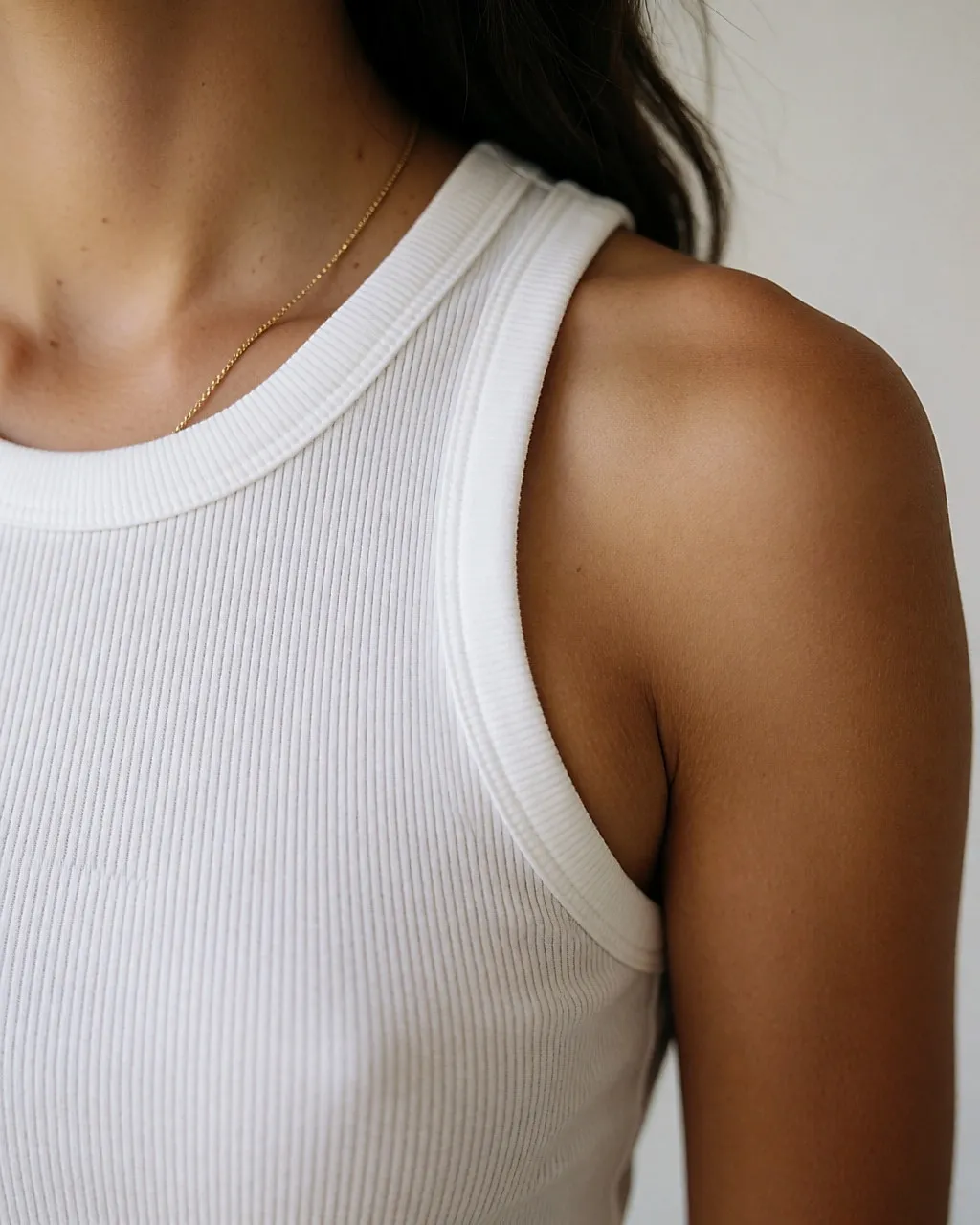 Detalle de un escote redondo de camiseta de tirantes blanca colocado por debajo de la clavícula