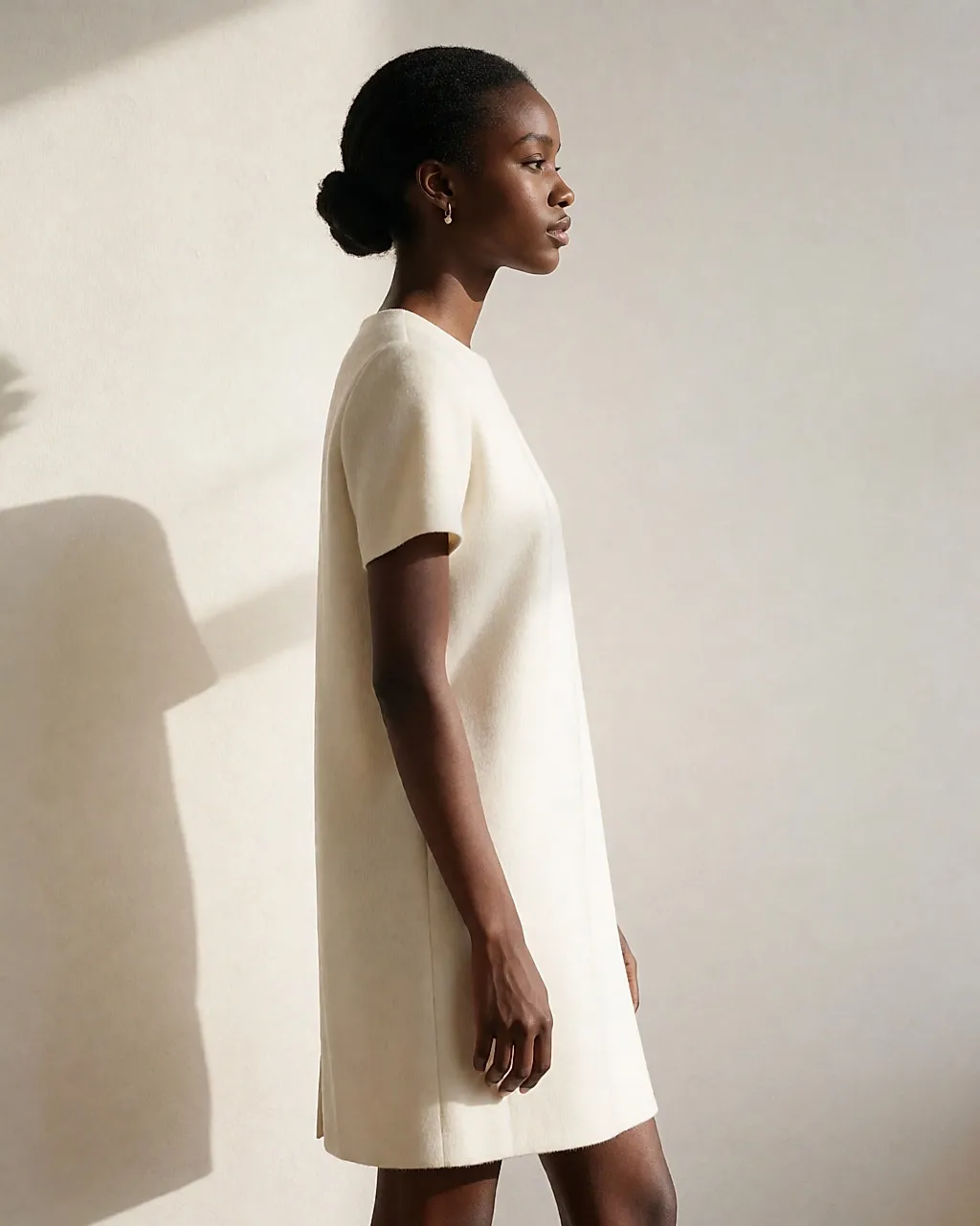 Model im Profil in elfenbeinfarbenem Trägerkleid vor heller Wand