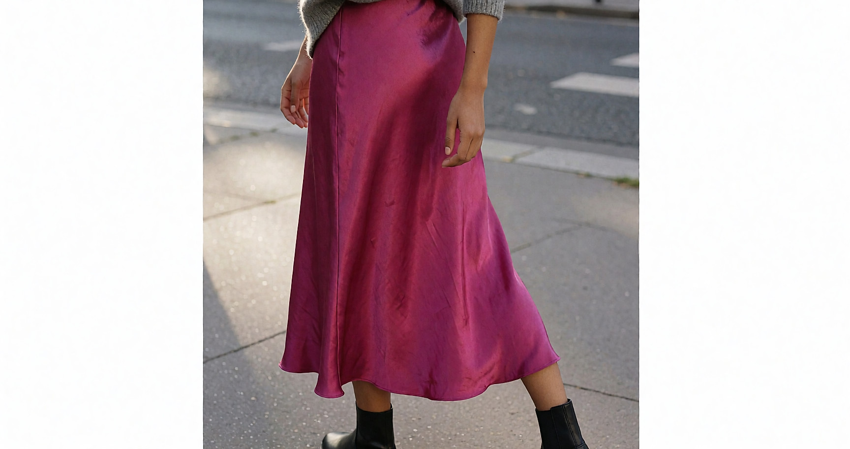 Jeune femme de dos marchant dans la rue, jupe midi satinée fuchsia et grosse maille grise