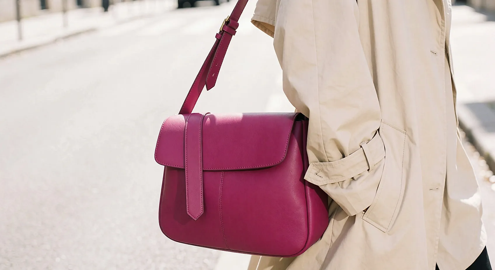 Junge Frau von hinten mit strukturierter Fuchsia-Ledertasche, beigem Trenchcoat und schwarzer Hose