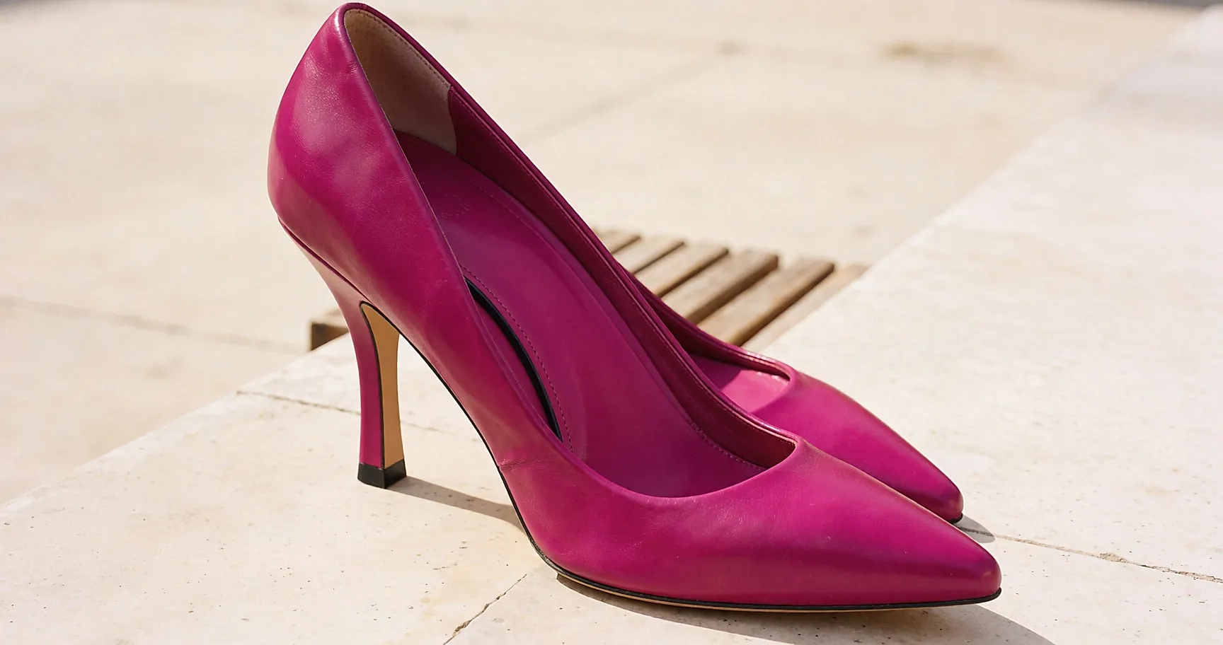 Fuchsia-Lederschuhe zu einer schwarzen Hose mit geradem Schnitt, übereinandergeschlagene Beine auf einer Bank
