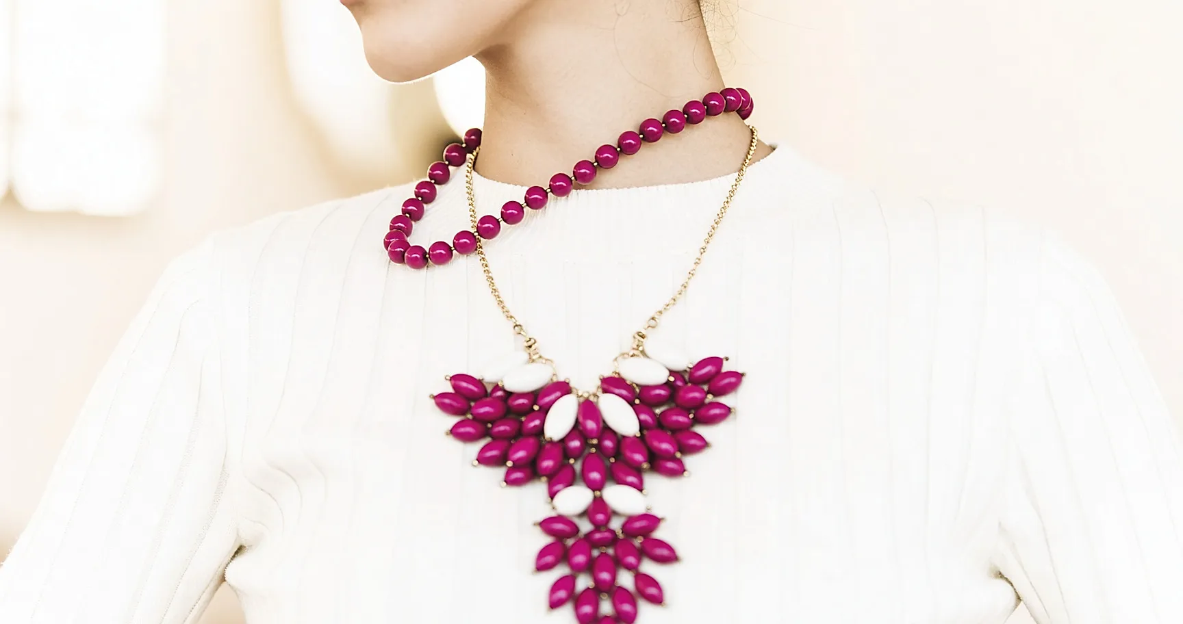 Große Fuchsia-Perlenkette auf cremefarbenem Strick, Bildausschnitt Schultern und Hals