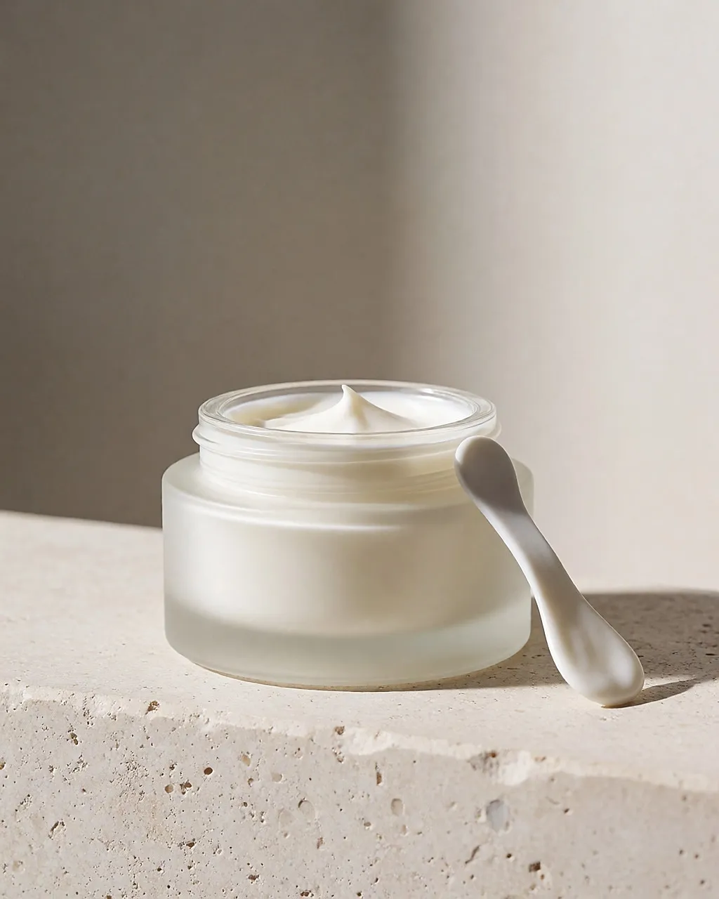 Mattes Glasgefäß mit glättender Creme und Spatel auf einer hellen Ablage.