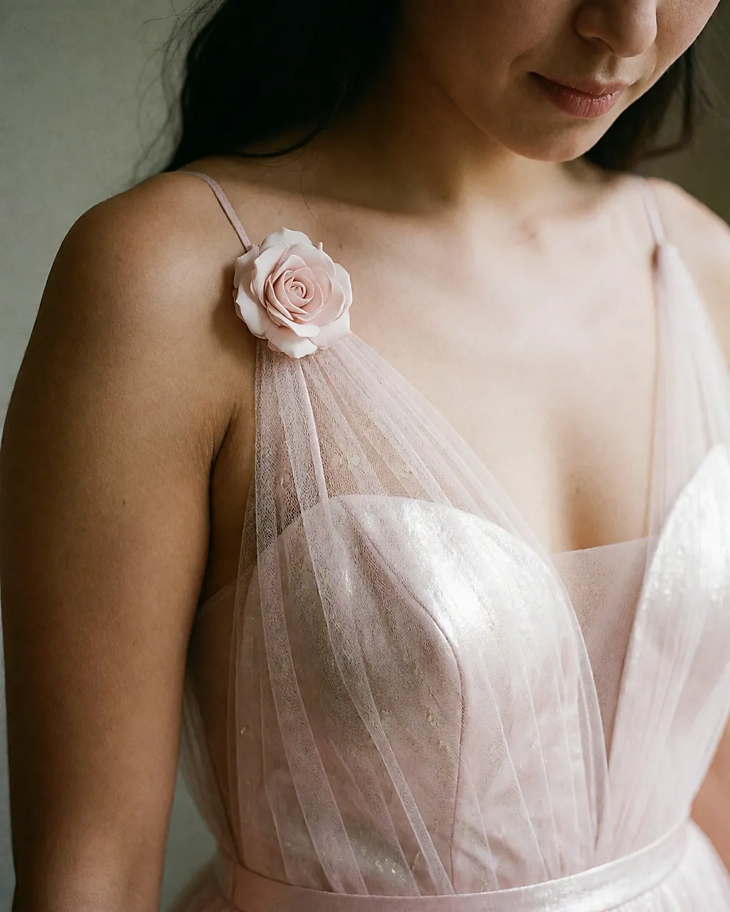 Detail of a barely pink wedding dress with a flower on the strap and luminous tulle