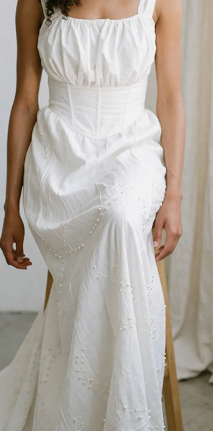 Seated bride in a bohemian dress with a lightly puffed bodice and a skirt embroidered with pearls