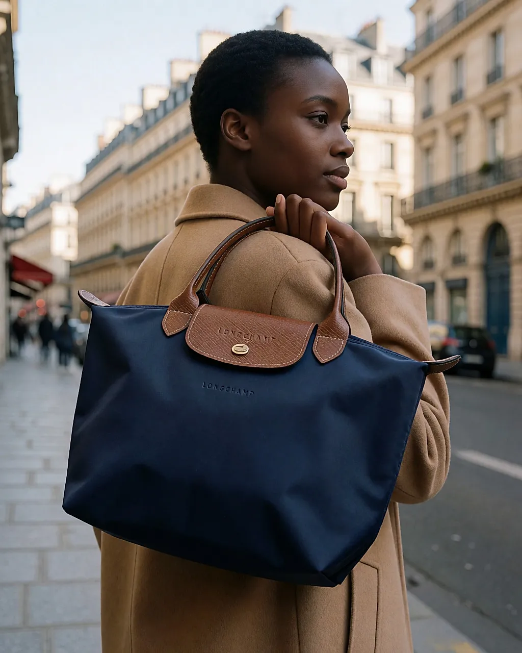 Eine Frau von hinten trägt ein dunkelblaues Longchamp Le Pliage über der Schulter, in einer Straße