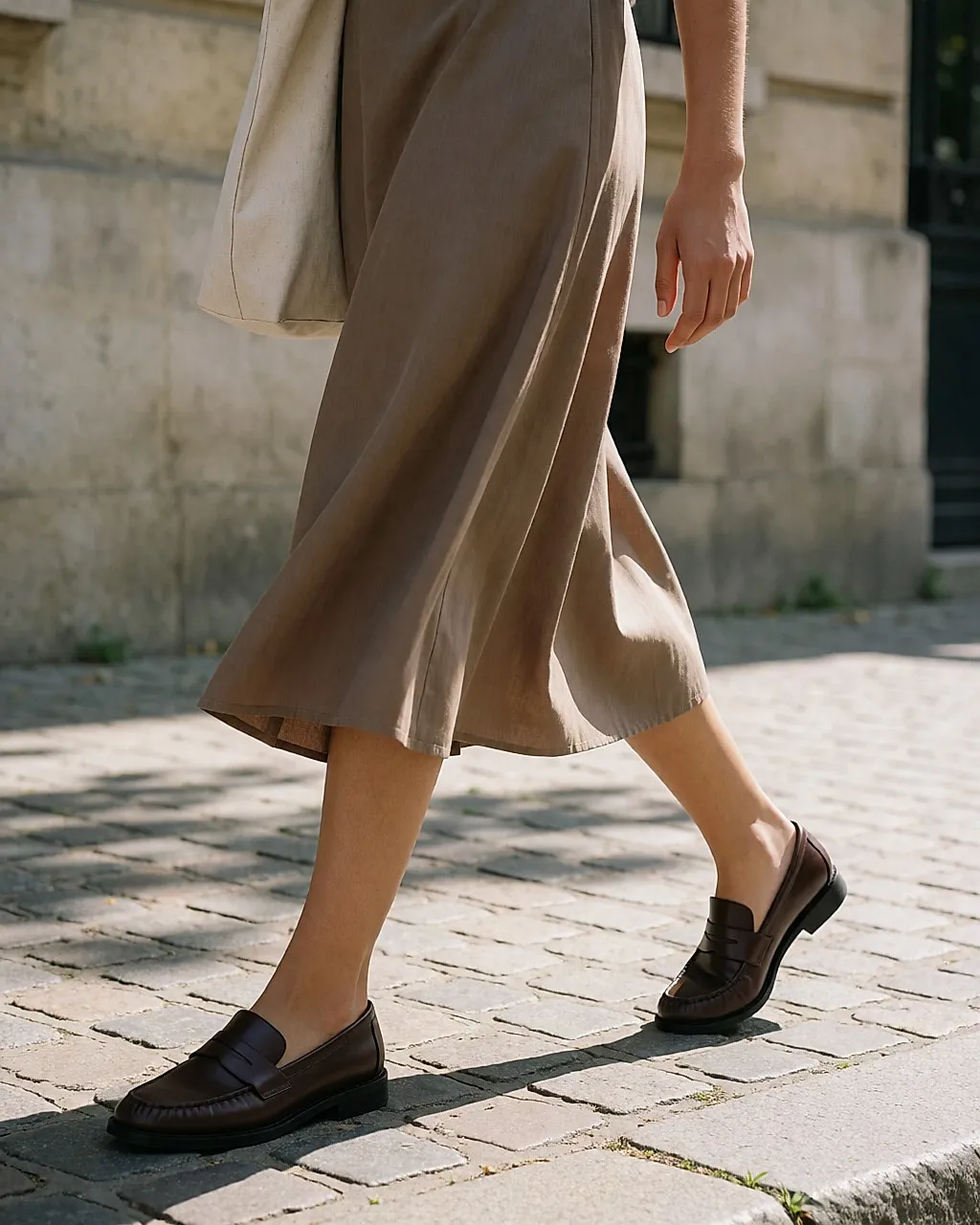 Brown leather loafers worn, midi skirt and sunny pavement, close crop