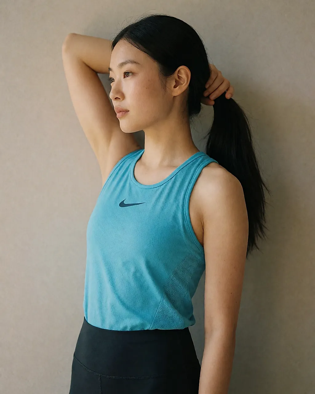 Top Nike turquoise porté par une femme devant un mur gris clair