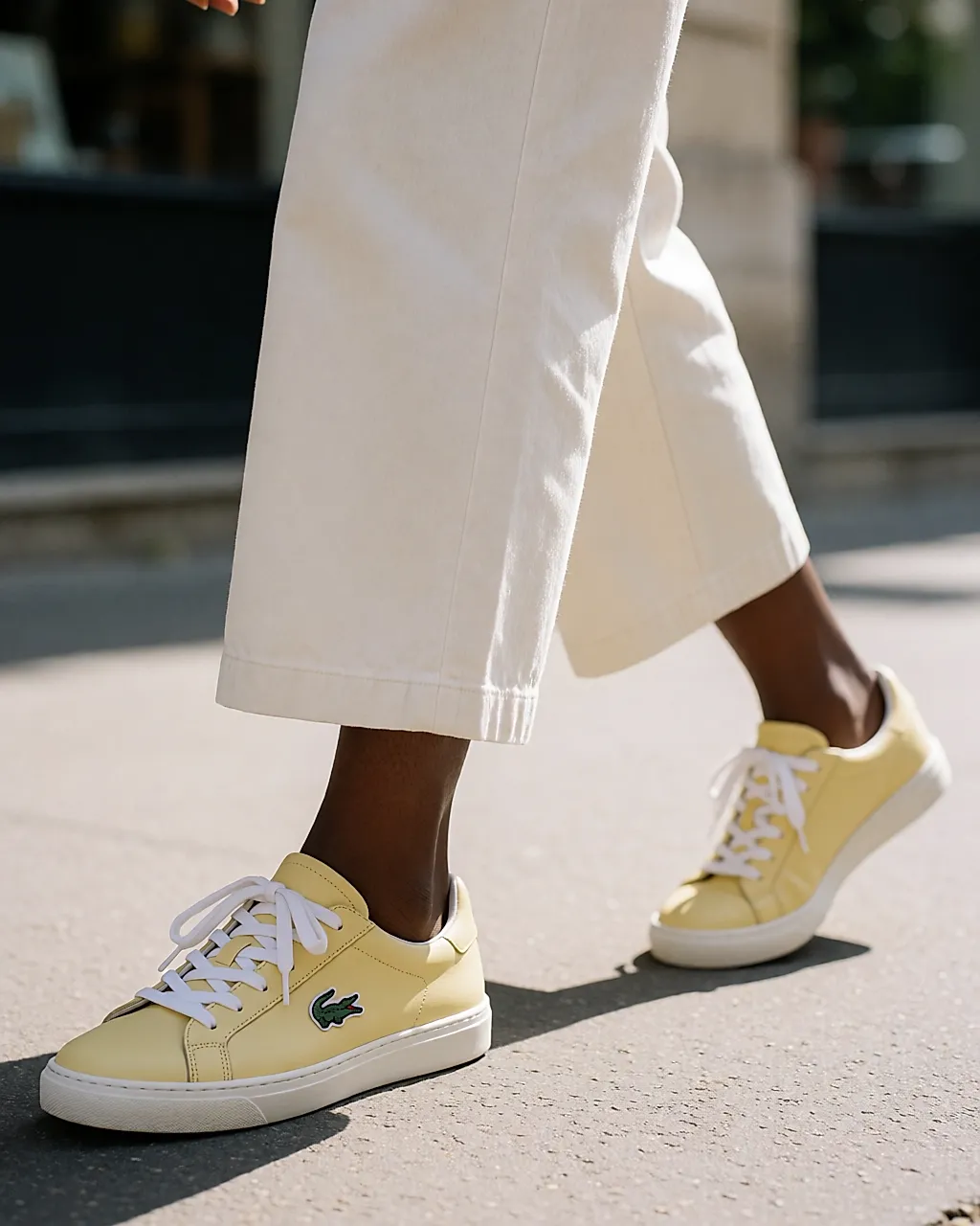 Low-top pale yellow trainers on a sunny pavement