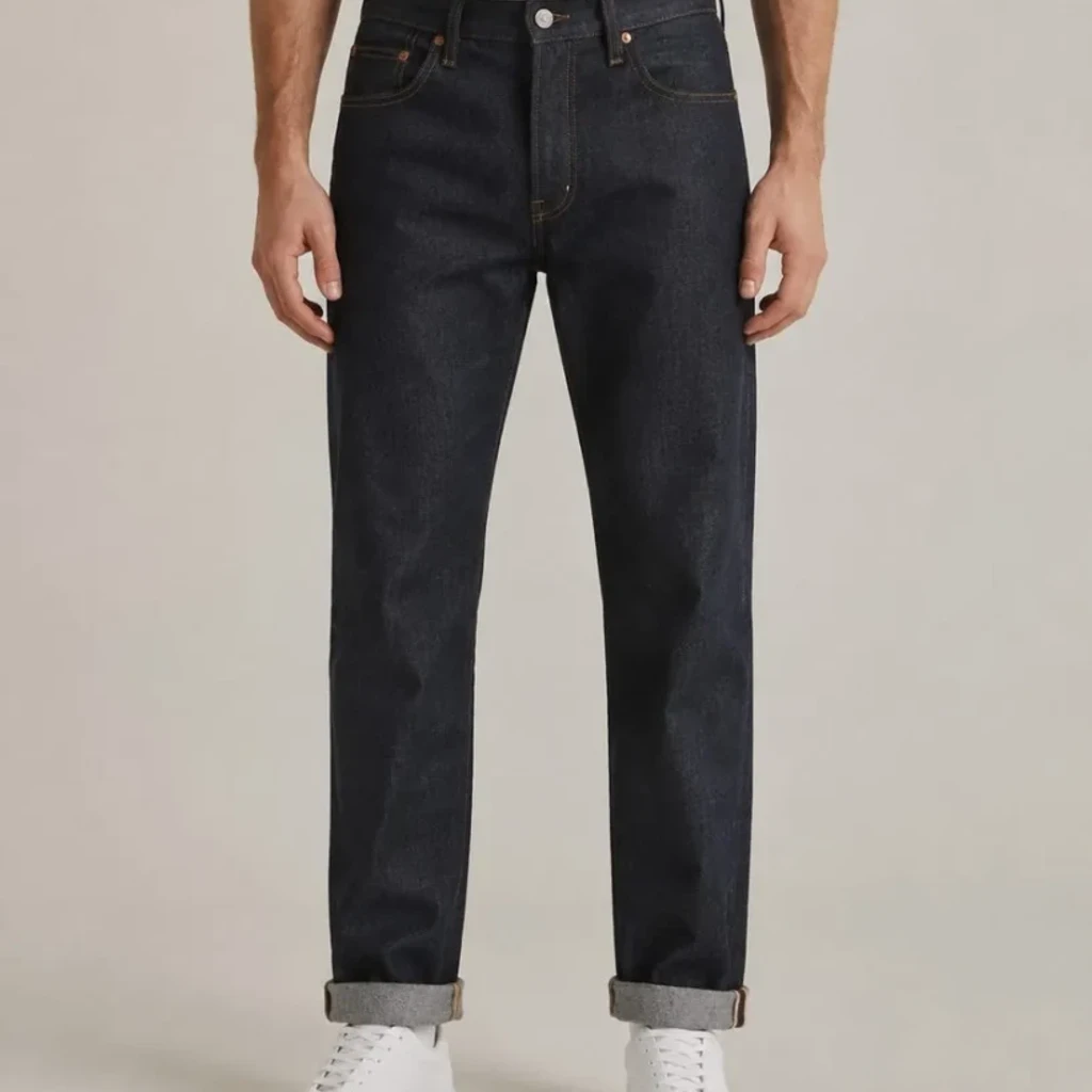 Vista de costas de uns jeans crus de perna direita usados com uma t-shirt branca por dentro