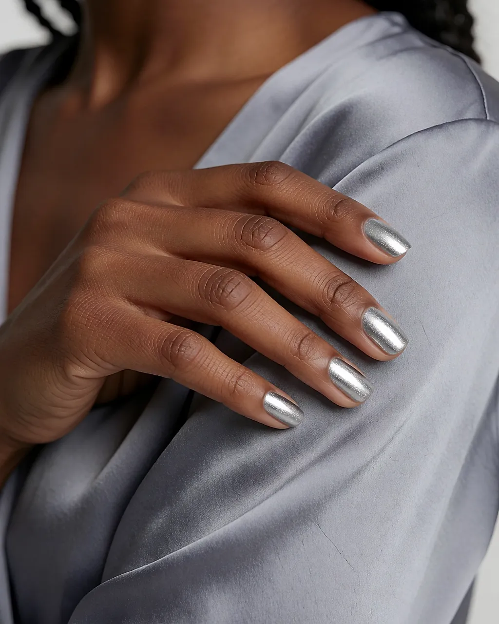 Une main aux ongles argentés pailletés posée sur un satin gris tourterelle